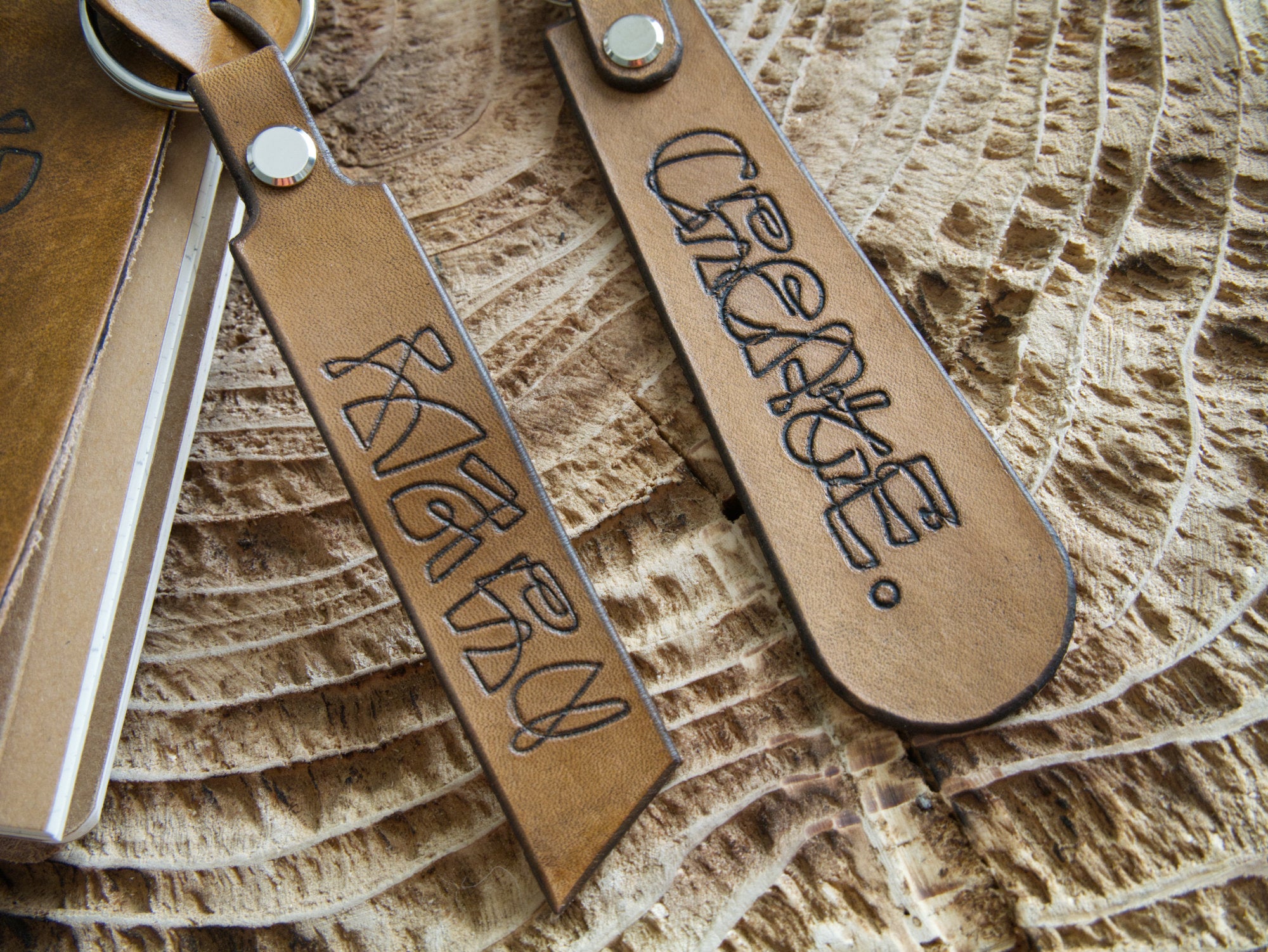 Two leather keychains with engraved text on a textured surface
