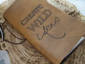 Brown leather notebook with 'Create Wild Ideas' text on a wooden surface
