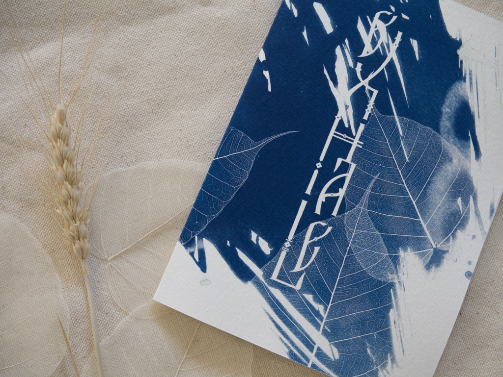 Blue and white abstract cyanotype greeting card with lettering Exhale on a textured beige surface with a dried leaf.