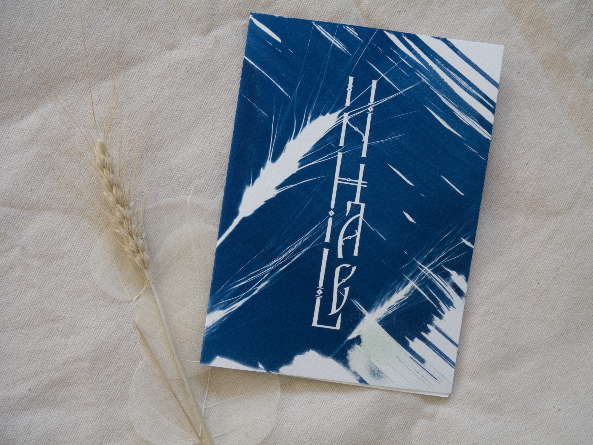 Blue and white abstract cyanotype greeting card with lettering Inhale on a textured beige surface