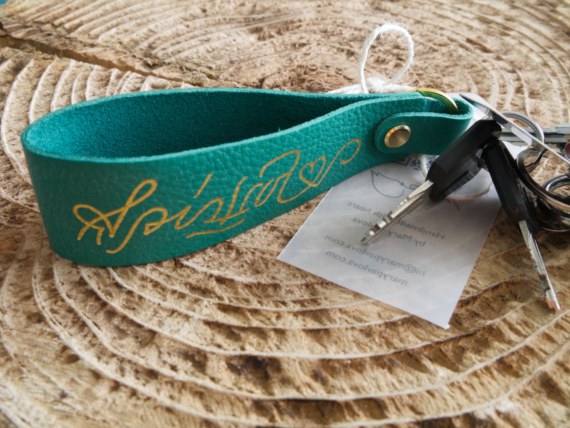 Green leather keychain with gold text on a wooden surface