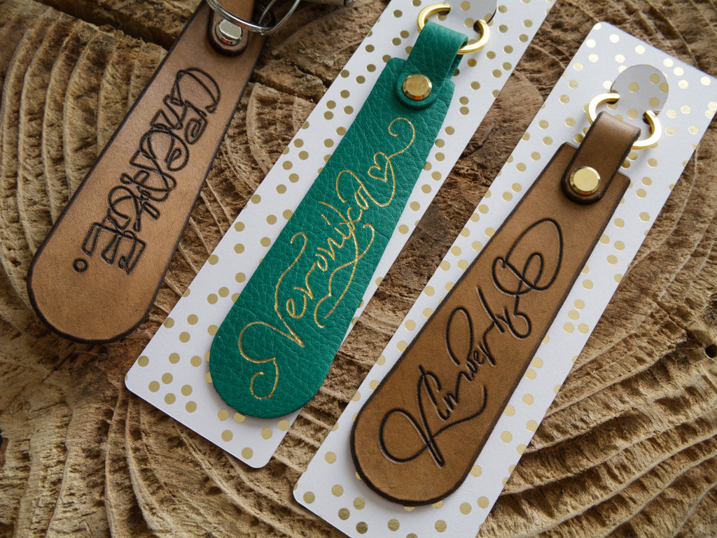 Three leather keychains with engraved text on a textured surface